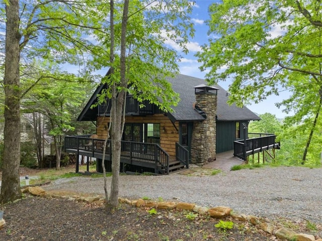 view of home's exterior with a chimney, a deck, and a shingled roof