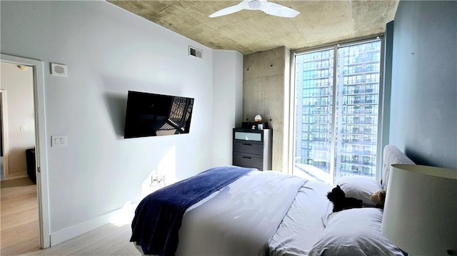 bedroom with visible vents, baseboards, ceiling fan, a wall of windows, and light wood-style flooring