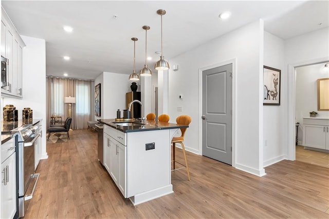 kitchen with a kitchen island with sink, white cabinets, a kitchen breakfast bar, sink, and decorative light fixtures