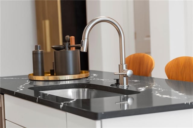 details featuring sink, white cabinetry, and dark stone countertops