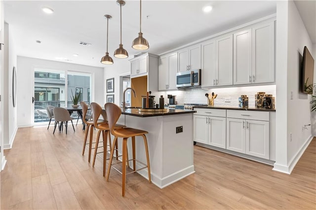 kitchen featuring decorative backsplash, decorative light fixtures, a center island with sink, and light hardwood / wood-style flooring