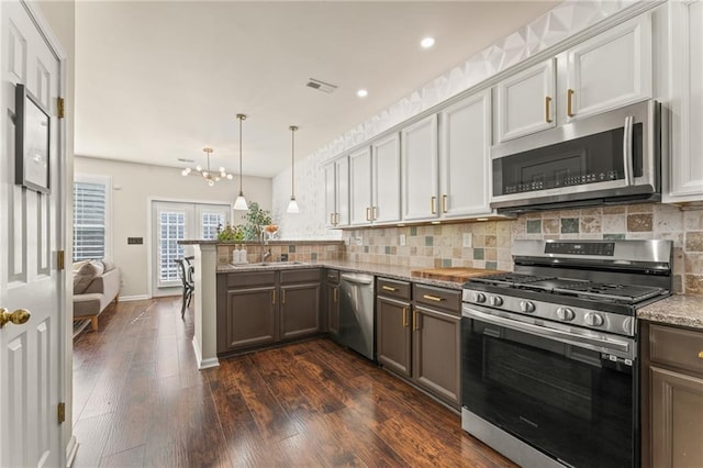 kitchen with appliances with stainless steel finishes, decorative light fixtures, backsplash, kitchen peninsula, and light stone countertops