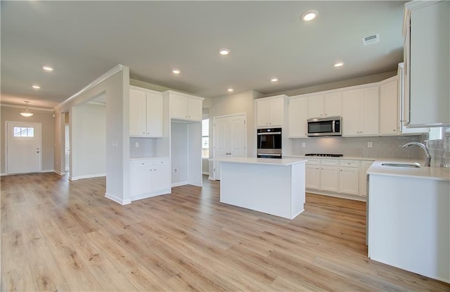 kitchen featuring light wood finished floors, a center island, a sink, stainless steel appliances, and backsplash