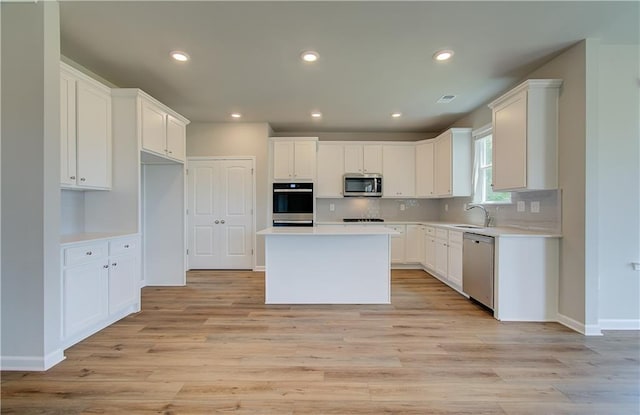 kitchen featuring stainless steel appliances, a kitchen island, white cabinets, light wood-style floors, and decorative backsplash