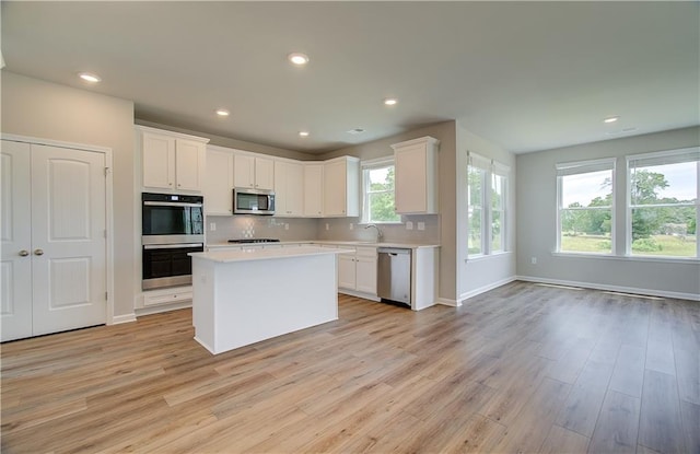 kitchen featuring white cabinetry, light countertops, appliances with stainless steel finishes, backsplash, and light wood finished floors