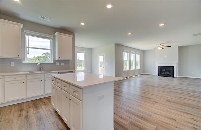 kitchen featuring visible vents, a glass covered fireplace, light countertops, light wood-type flooring, and a sink