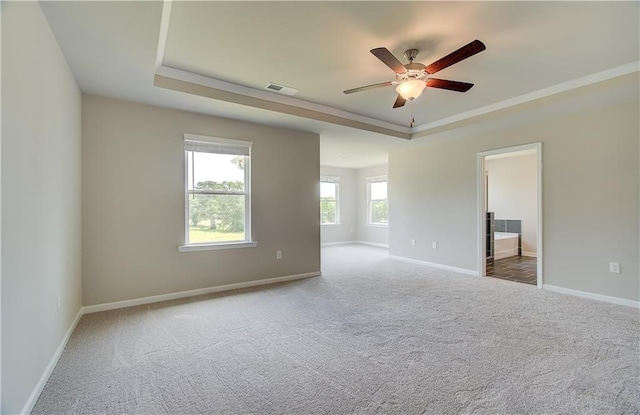 carpeted empty room with ceiling fan, visible vents, baseboards, ornamental molding, and a raised ceiling