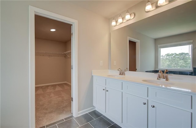 bathroom with double vanity, a spacious closet, tile patterned flooring, and a sink