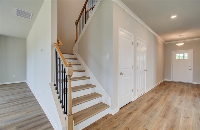 entryway featuring light wood-style floors, baseboards, visible vents, and crown molding