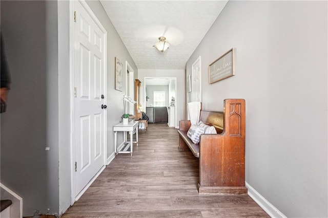 hall featuring a textured ceiling, baseboards, and wood finished floors