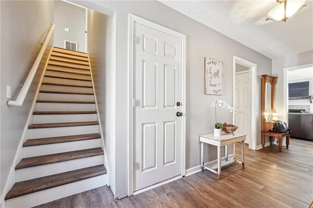 entryway with stairs, visible vents, baseboards, and wood finished floors