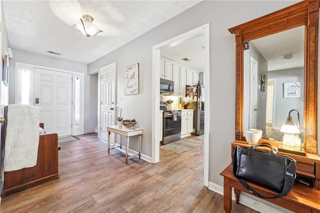 entryway with a textured ceiling, light wood finished floors, visible vents, and baseboards