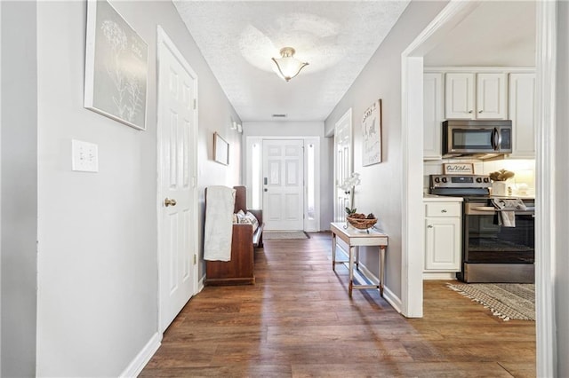 corridor featuring a textured ceiling, baseboards, and wood finished floors