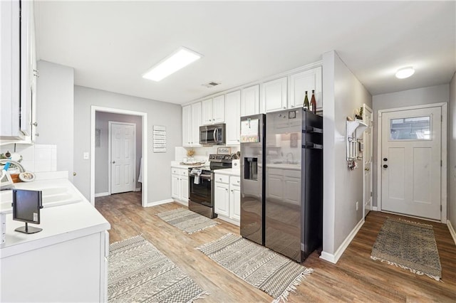 kitchen with stainless steel appliances, white cabinetry, a sink, and light wood finished floors