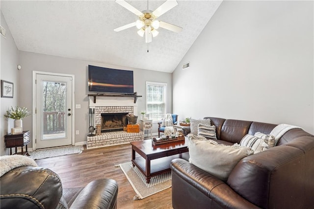 living area featuring a fireplace, wood finished floors, visible vents, baseboards, and a ceiling fan