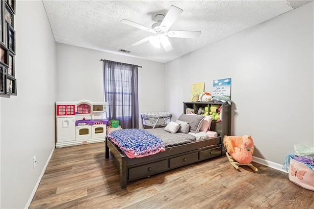 bedroom with a ceiling fan, a textured ceiling, visible vents, and wood finished floors