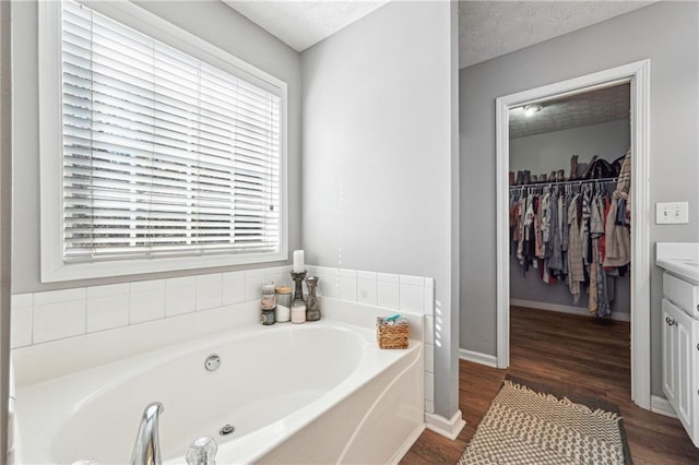 full bathroom featuring a textured ceiling, wood finished floors, vanity, a bath, and a walk in closet