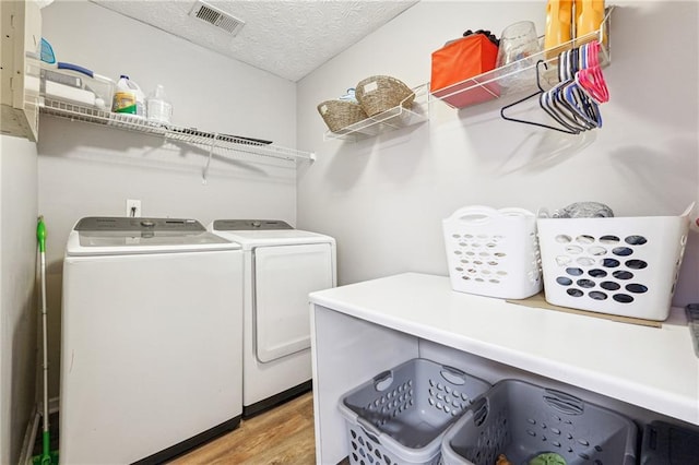 laundry room featuring visible vents, light wood-style floors, washing machine and dryer, a textured ceiling, and laundry area