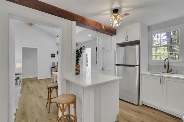 kitchen with sink, a breakfast bar area, stainless steel refrigerator, white cabinets, and beamed ceiling