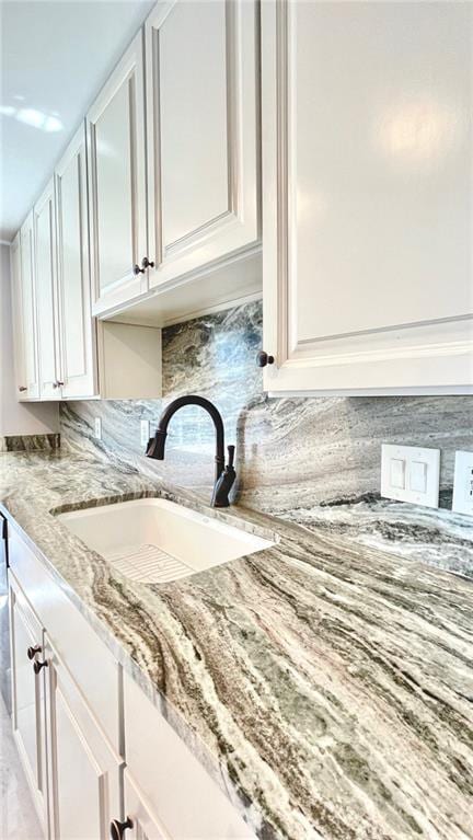 interior details featuring a sink, backsplash, white cabinetry, and light stone counters