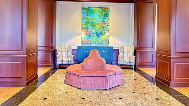sitting room with a decorative wall, granite finish floor, and a wainscoted wall