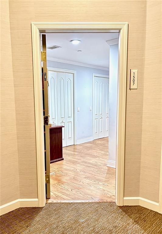 hall with crown molding, baseboards, visible vents, and light wood-type flooring