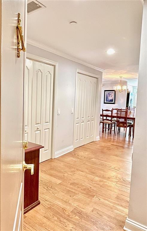 hall featuring crown molding, light wood-style flooring, visible vents, baseboards, and a notable chandelier
