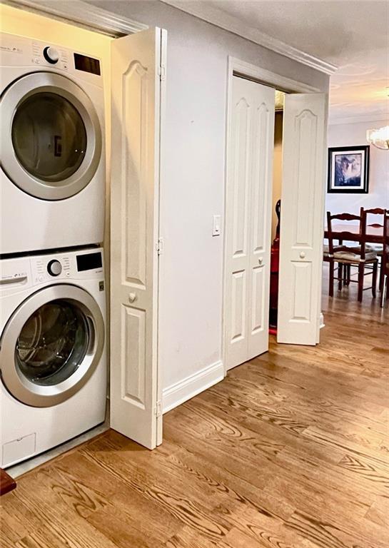 laundry area featuring baseboards, light wood-type flooring, a chandelier, laundry area, and stacked washer and dryer