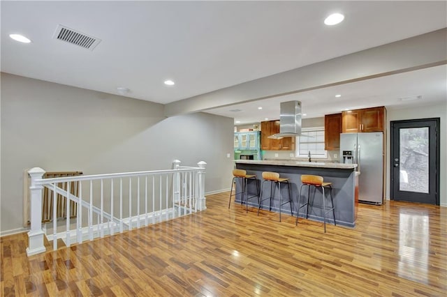 kitchen featuring a breakfast bar area, a kitchen island, visible vents, stainless steel fridge with ice dispenser, and island exhaust hood