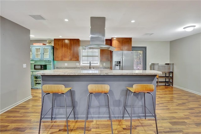 kitchen featuring island range hood, stainless steel fridge with ice dispenser, light countertops, light wood-type flooring, and a center island