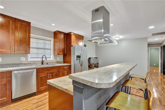 kitchen with a breakfast bar, a sink, light countertops, appliances with stainless steel finishes, and island exhaust hood