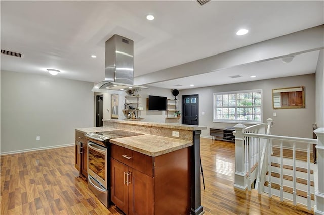 kitchen featuring island range hood, visible vents, open floor plan, electric stove, and light wood finished floors