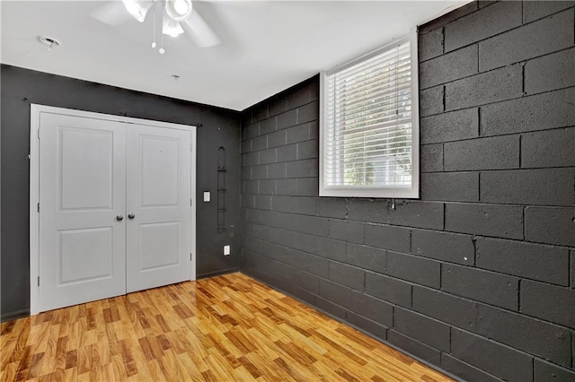 interior space with concrete block wall, light wood finished floors, and a ceiling fan