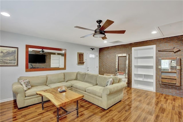 living area featuring light wood-style floors, brick wall, built in shelves, and attic access