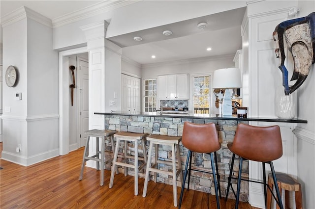 kitchen with white cabinets, backsplash, kitchen peninsula, and hardwood / wood-style floors