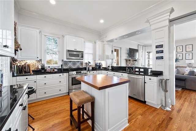 kitchen with decorative backsplash, appliances with stainless steel finishes, a kitchen island, white cabinetry, and a breakfast bar area