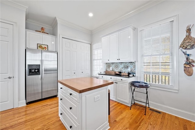 kitchen with white cabinetry, stainless steel fridge, crown molding, light hardwood / wood-style floors, and a kitchen island