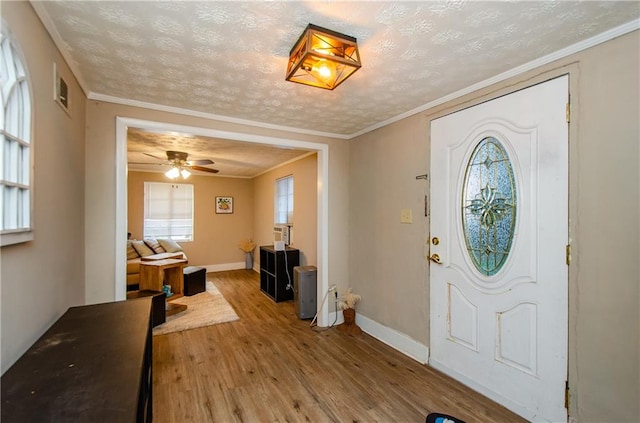 foyer entrance featuring ceiling fan, hardwood / wood-style flooring, ornamental molding, and a textured ceiling