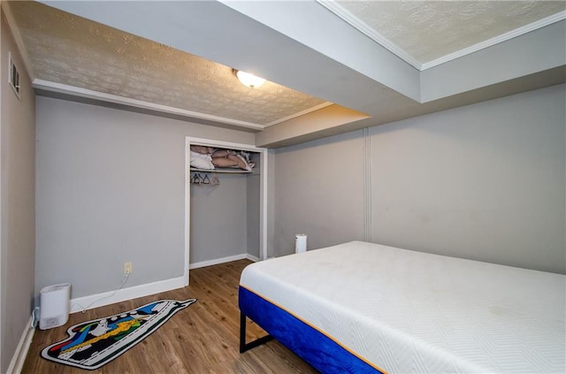 bedroom with ornamental molding, a textured ceiling, wood-type flooring, and a closet