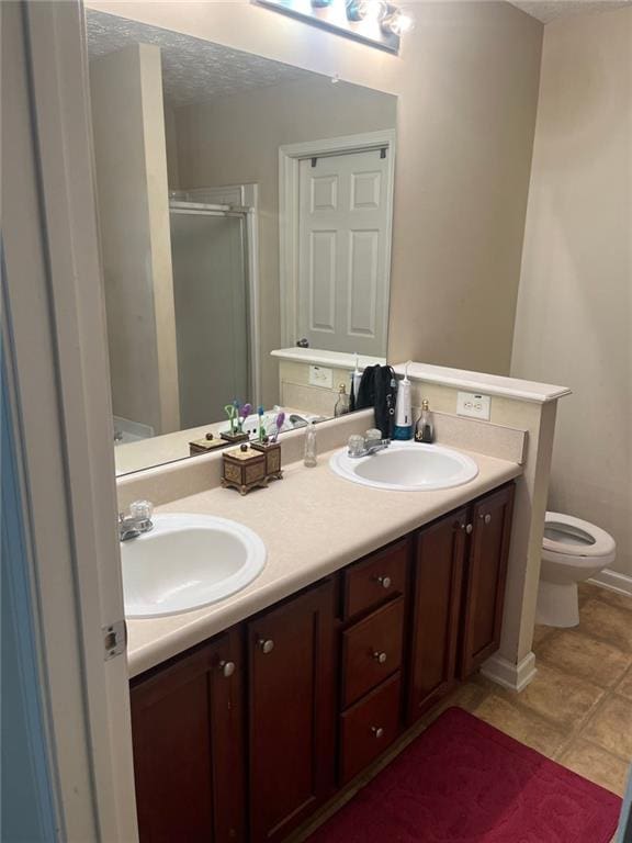 bathroom featuring a shower with door, vanity, a textured ceiling, tile patterned floors, and toilet