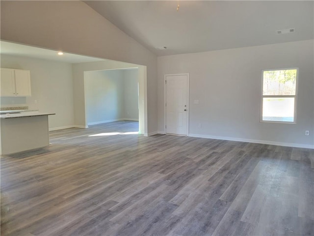 unfurnished living room with lofted ceiling, wood finished floors, visible vents, and baseboards