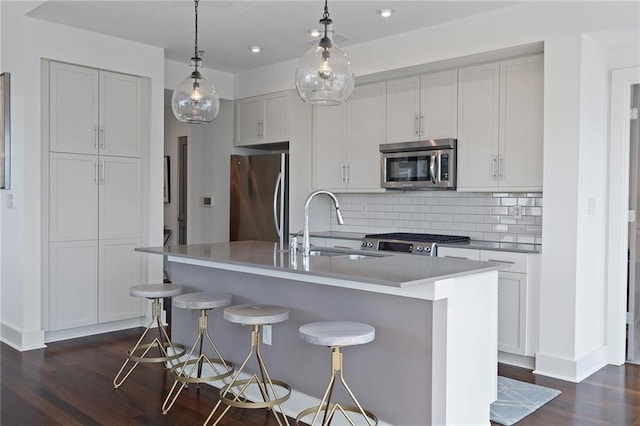 kitchen with a kitchen island with sink, hanging light fixtures, stainless steel appliances, dark wood-type flooring, and a breakfast bar