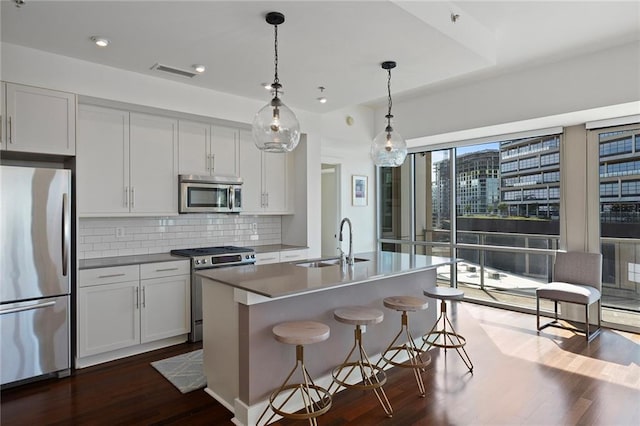 kitchen with pendant lighting, sink, dark wood-type flooring, appliances with stainless steel finishes, and a center island with sink