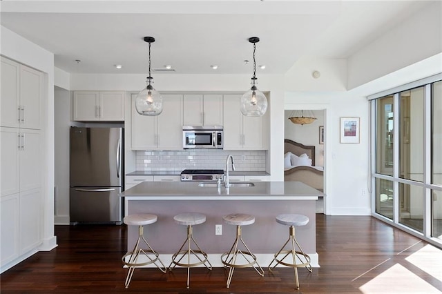 kitchen with decorative light fixtures, an island with sink, dark wood-type flooring, appliances with stainless steel finishes, and a breakfast bar area