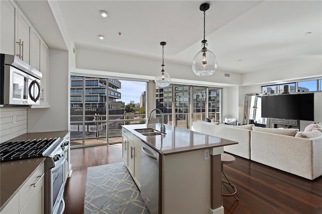 kitchen featuring a kitchen island with sink, white cabinetry, stainless steel appliances, sink, and dark wood-type flooring