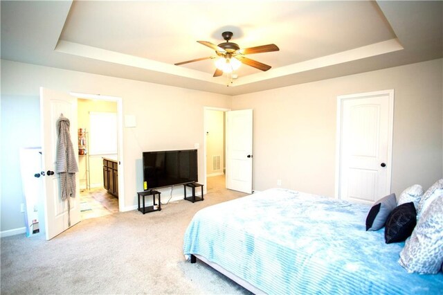 carpeted bedroom with a tray ceiling, a ceiling fan, visible vents, and baseboards