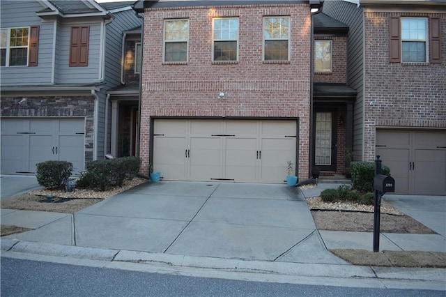 townhome / multi-family property with a garage, driveway, and brick siding