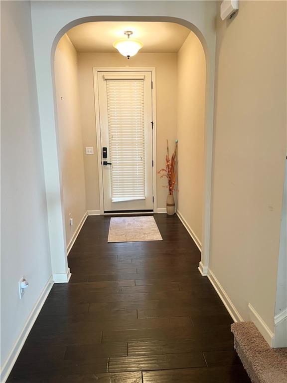 doorway featuring baseboards, arched walkways, and dark wood-style flooring