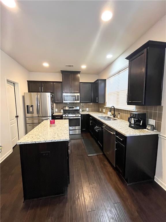 kitchen featuring light stone counters, dark wood-style flooring, appliances with stainless steel finishes, a sink, and a kitchen island