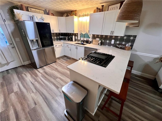 124 Dockside Downs Dr, Woodstock, GA 30189 - kitchen with appliances with stainless steel finishes, a peninsula, light countertops, white cabinetry, and backsplash